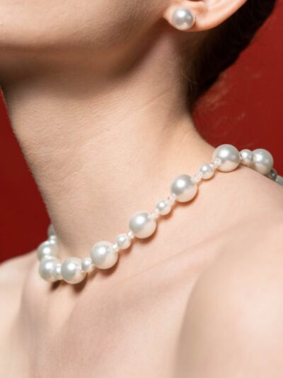 Close-up of a woman's neck adorned with a pearl necklace against a red background.